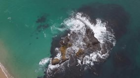 Aerial top-down view of waves crashing against a rocky outcrop in turquoise coastal waters - Powered by Shutterstock - Get 15% off with code: PIKWIZARD15
