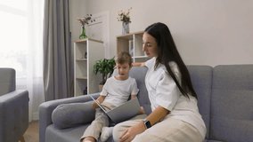 Seven year old boy reading book while sitting on sofa with his mother listening beside him, spending quiet family time and learning together at home - Powered by Shutterstock - Get 15% off with code: PIKWIZARD15