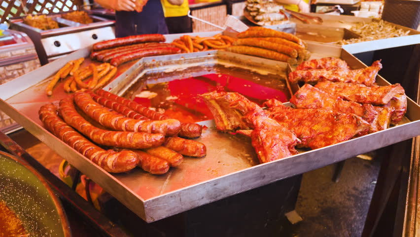 Vibrant scene at a street food stall of a traditional market, containing sausages and other types of meats and street food meals
