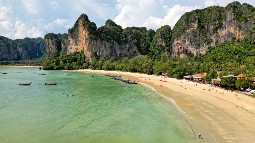 Aerial view of the turquoise waters meeting the sandy shore of Railay Beach, framed by towering cliffs and lush greenery, Ao Nang, Krabi, Thailand.