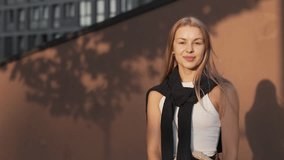 Caucasian woman with long straight hair wearing white top. Standing outdoors while holding shopping bags. Smiling softly and raising hand with gesture of satisfaction. Enjoying successful purchases. - Powered by Shutterstock - Get 15% off with code: PIKWIZARD15