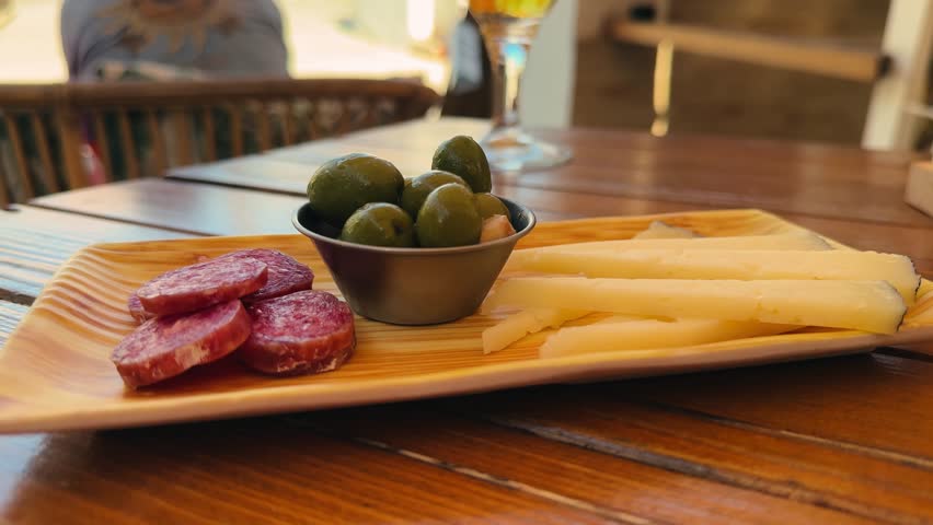 Wooden plate with a set of snacks for beer or wine Spanish sausage fuet, pieces of cheese, and green olives.