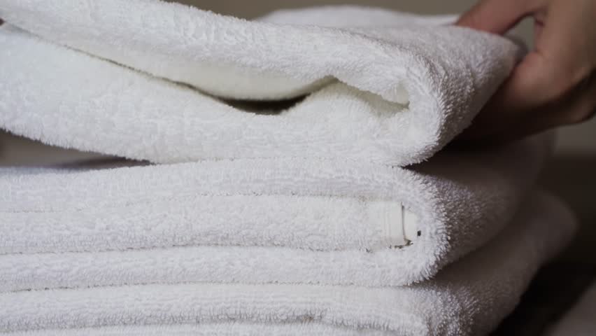 Close-up of hands placing white bath towels on the bed sheet. Concept of room cleaning service.