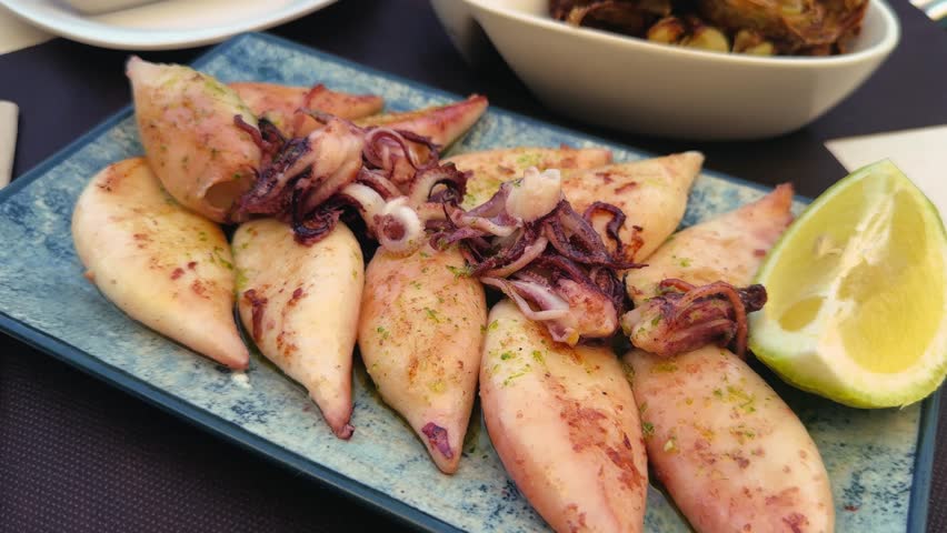 Baby squid in basil sauce with lemon sprinkles on a plate at a snack bar.