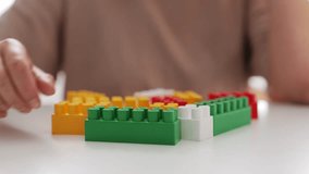 A hand is stacking green and yellow building blocks while other colorful blocks sit nearby on a table, showcasing creativity during playtime - Powered by Shutterstock - Get 15% off with code: PIKWIZARD15