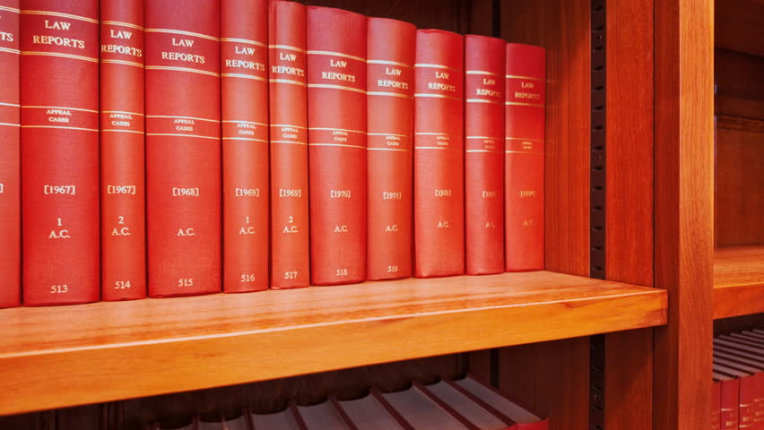 Close up of various red law books containing reports of important legal cases, stacked on a shelf with gilt titles and pristine spines