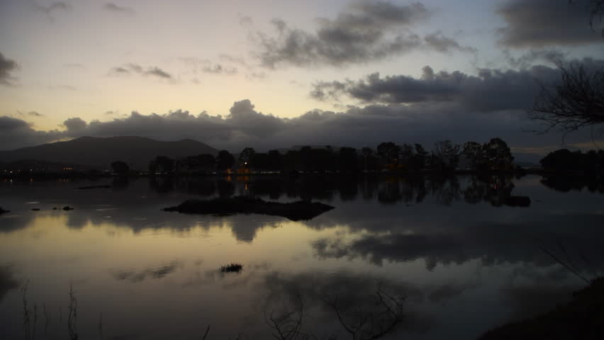 A predawn pan clip of a wetland wildlife habitat with beautiful light and cloud reflections on the still water.