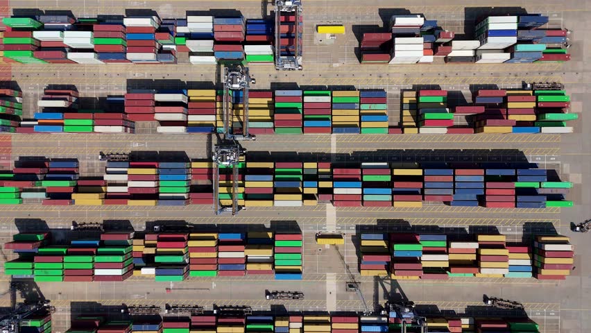 Top down aerial drone shot of busy shipping container port, rows of coloured containers being loaded and unloaded onto cargo ships by gantry cranes and trucks on a sunny summer day in Felixstowe, Unit