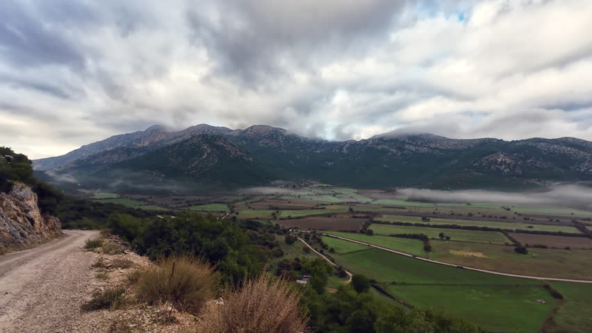 A high angle pan clip of a mountain valley farm land in morning mist.