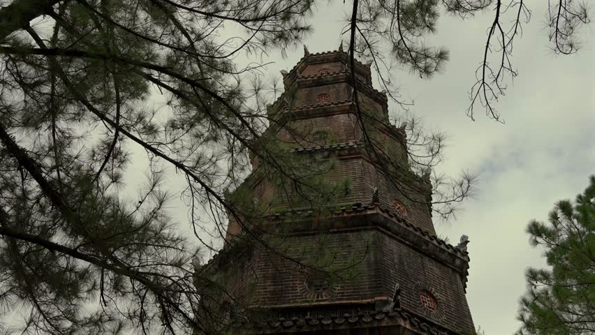 a historic temple hall at Thien Mu Pagoda, Hue, Vietnam, featuring a dark tiled roof and classic wooden architecture, partially obscured by tall cypress trees