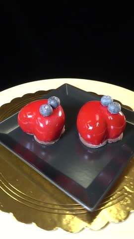Heart-shaped cookies with glossy coating decorated with blueberries rotate on a black plate