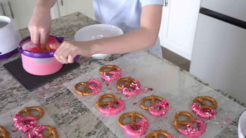With focused attention, this budding culinary artist dips pretzels into a pot of melted chocolate, creating sweet delights in the warmth of a well-lit home kitchen.