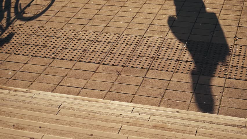 Pedestrian and bicycle shadow on textured sidewalk in warm evening light. 4K with selective focus.