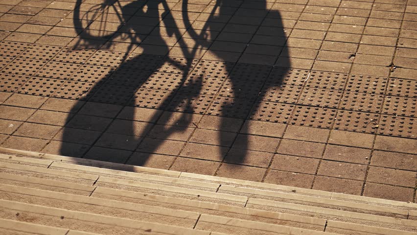 Pedestrian and bicycle shadow on textured sidewalk in warm evening light. 4K with selective focus.