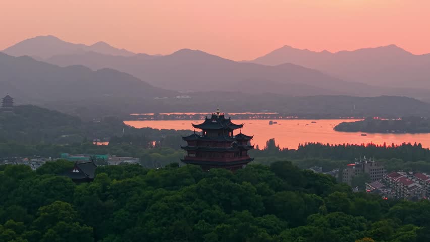 Aerial view of Chenghuang pagoda at sunset over Xihu lake in Hangzhou featuring mountains and lush green trees