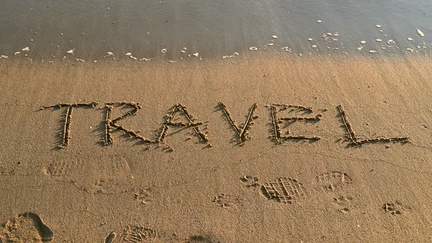 The word “TRAVEL” written on sandy beach near the shoreline