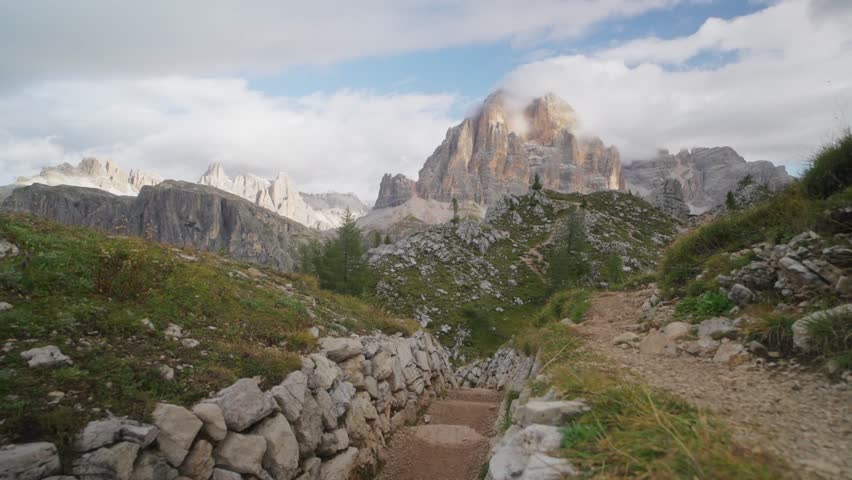 Male hiker wearing a yellow jacket and backpack walking along a mountain trail in the Dolomites, Italy. Adventure travel and exploration in the Alps