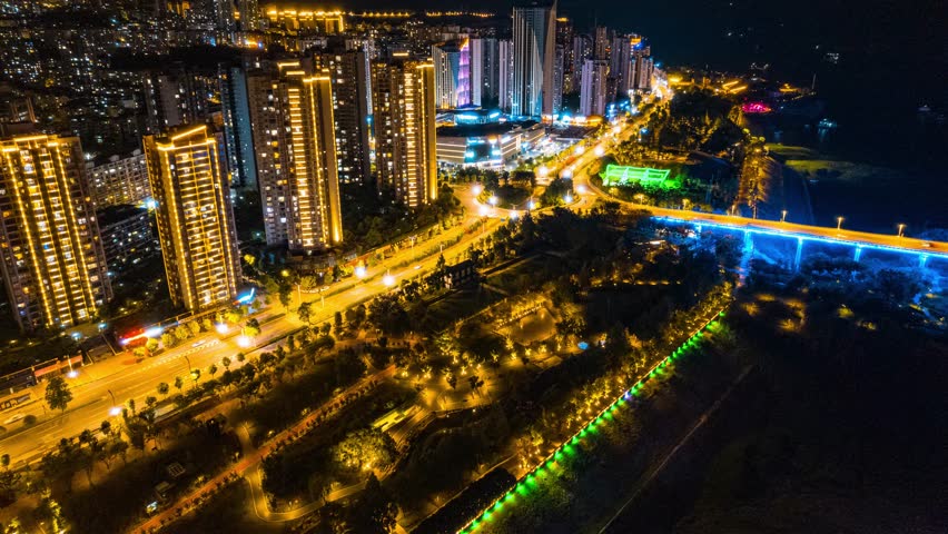 Stunning aerial night view of Yunyang cityscape in Chongqing, China showcasing illuminated skyscrapers, colorful bridges, and urban infrastructure in golden hour lighting.