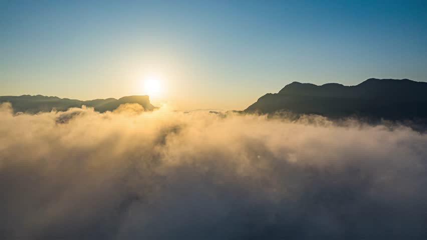 Aerial time lapse of sunrise over Three Gorges region with golden clouds flowing between mountain peaks and Yangtze River valley below in China