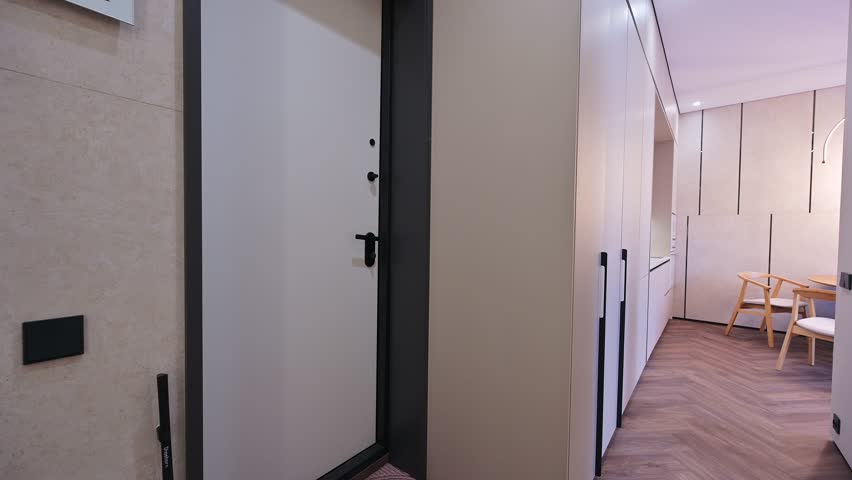 minimalist interior featuring white walls, built-in cabinets with long handles, and a herringbone wood floor. A door with a black handle is partially open, leading to a dining area