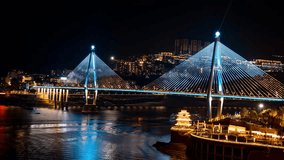 Time lapse night view of illuminated cable-stayed bridge over Yangtze River in Badong County, China with city skyline and traditional architecture reflected in water. - Powered by Shutterstock - Get 15% off with code: PIKWIZARD15