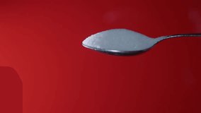 Sugar pouring from a spoon against a vibrant red background in a close-up shot capturing the texture and movement of the granules - Powered by Shutterstock - Get 15% off with code: PIKWIZARD15