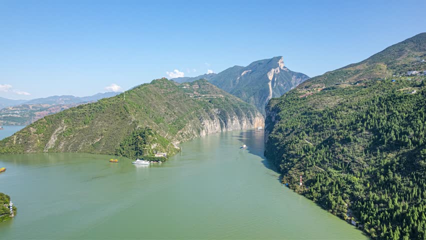 Aerial view of Qutang Gorge in Chongqing, China showing dramatic limestone cliffs, green mountains, and Yangtze River with boats navigating the scenic waterway.