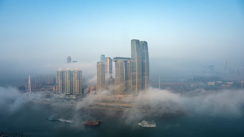 Aerial view of Chongqing city skyline emerging through dramatic fog and mist, showcasing modern skyscrapers and urban development in this major Chinese metropolis.
