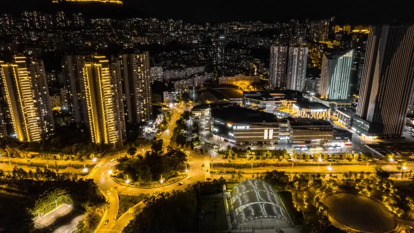 Stunning aerial night time lapse view of Yunyang County in Chongqing, China showcasing illuminated skyscrapers, traffic flow, and urban development with golden lighting.