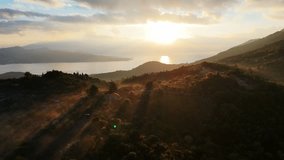 A backward aerial drone footage of the rising sun breaking through the clouds over the sea horizon to cast its golden light over a misty mountain valley and creating long shadows on the landscape. - Powered by Shutterstock - Get 15% off with code: PIKWIZARD15