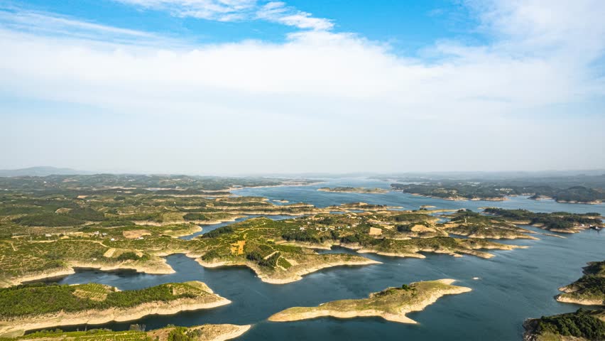 Aerial panoramic view of Danjiangkou Reservoir showing blue water, white clouds, and vast landscape under dramatic sky in time lapse style
