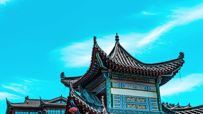 Traditional Chinese pagoda with ornate curved rooflines and decorative details against a bright blue sky with white clouds, showcasing ancient Asian architectural style.
