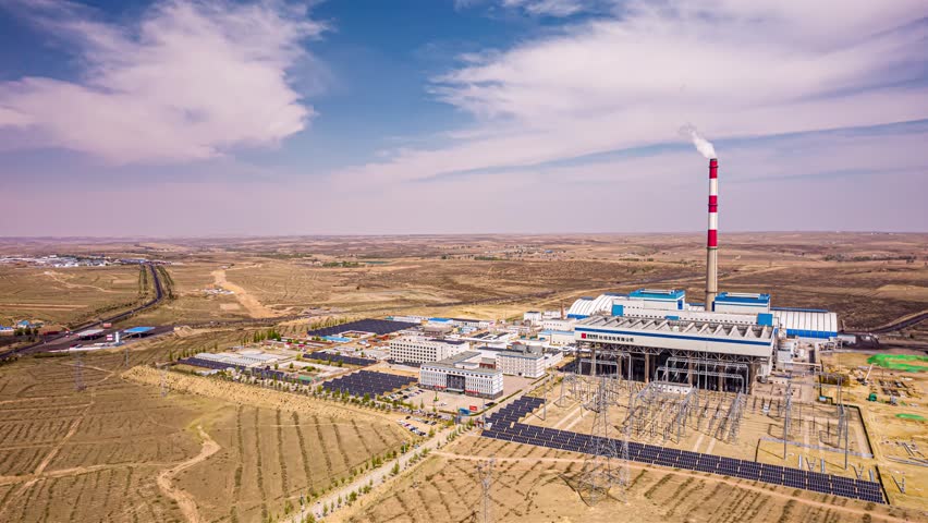Aerial view of coal-fired power station with solar photovoltaic panels in Inner Mongolia grassland landscape under blue sky with white clouds