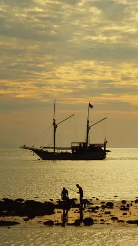 Terengganu, Malaysia - 31 October 2025 : A medium-sized fishing boat by the beach during sunset, surrounded by calm sea and warm orange evening light.