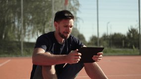 Caucasian man sits on outdoor sports field, emotionally celebrating favorite team victory. Fan watches sports match on tablet and celebrates winning bet. - Powered by Shutterstock - Get 15% off with code: PIKWIZARD15