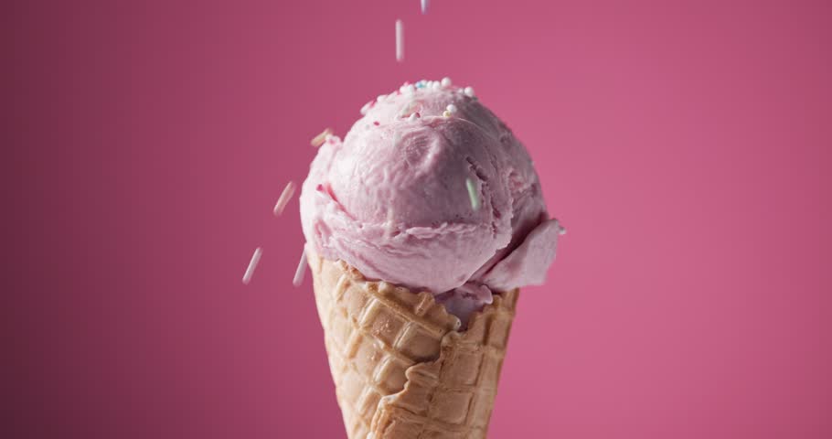 scoop of strawberry ice cream in a waffle cone rotating against a pink background, decorative sugar sprinkles falling on an icecream ball 
