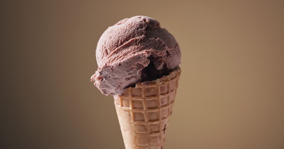 scoop of chocolate ice cream in a waffle cone rotating against a brown background