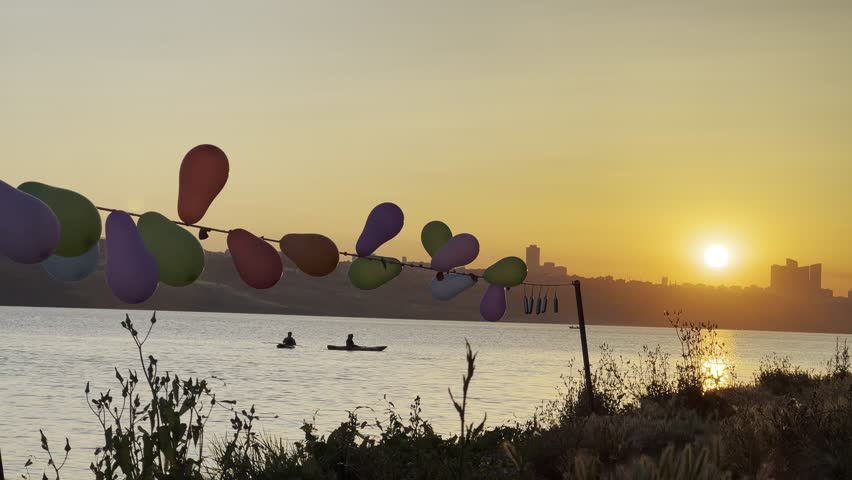 ISTANBUL, TURKEY - SEPTEMBER 8, 2025: Colorful balloons lined up on a string, set up as targets for a shooting game. The scene is silhouetted against the beautiful sunset sky.
