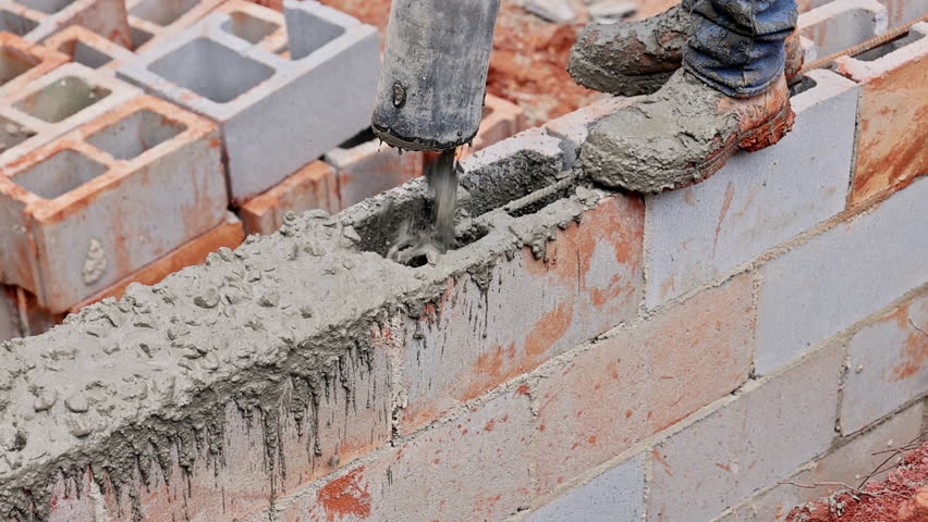 Worker uses concrete mixer to fill wet cement to cinder blocks on construction site