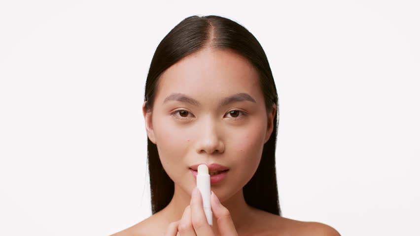 Young woman applying lip balm while pampering herself with skin care routine