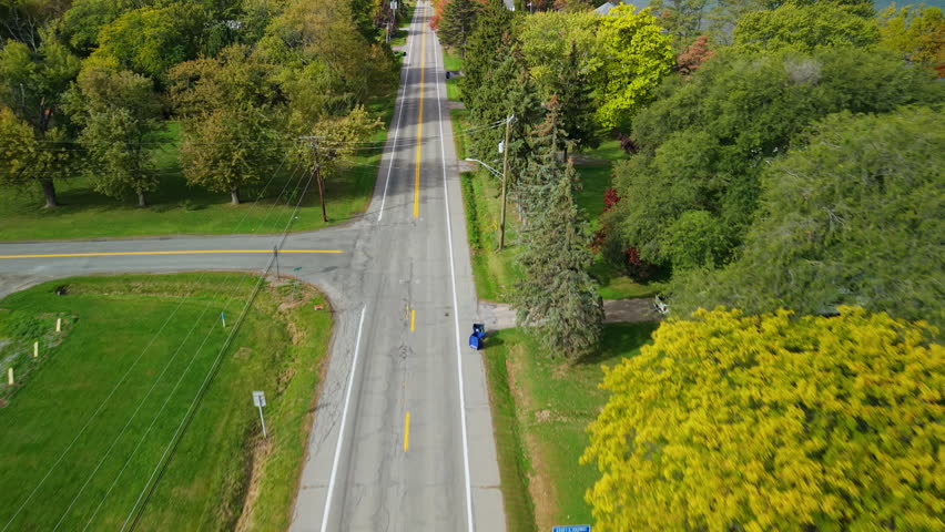 Aerial view of a typical American suburban road lined with green trees and lawns, showing a calm neighborhood intersection. High quality 4k footage