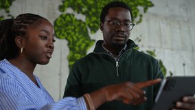 Young black business partners discussing a project on a digital tablet. Professional man and woman collaborating in an office with a world map - Powered by Shutterstock - Get 15% off with code: PIKWIZARD15