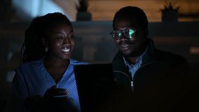 Professional african american colleagues working late in a dark office. Two happy business partners discussing a project on a digital tablet - Powered by Shutterstock - Get 15% off with code: PIKWIZARD15