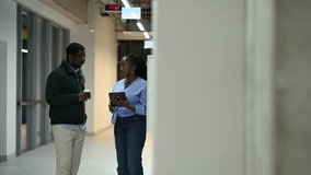 Two professional african american coworkers having a conversation in a modern office hallway. A woman holding a tablet is talking to a man - Powered by Shutterstock - Get 15% off with code: PIKWIZARD15