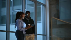Two young black business professionals discussing a project on a digital tablet. Man and woman coworkers brainstorming ideas in a modern corporate building at night - Powered by Shutterstock - Get 15% off with code: PIKWIZARD15