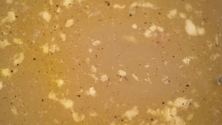 boiling, savory beef broth with spices and melting gelatin pieces being stirred with big metal spoon. close-up view cooking process for traditional rich beef jelly or savory aspic.