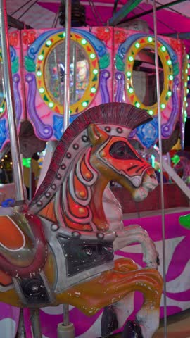 Creepy vintage carousel horse moving up and down at a funfair, illuminated by spooky colored lights