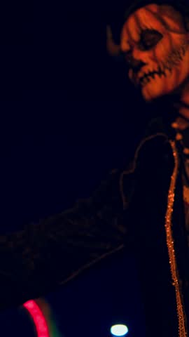 Creepy character in a pumpkin mask and horns holding a small gourd during a halloween event