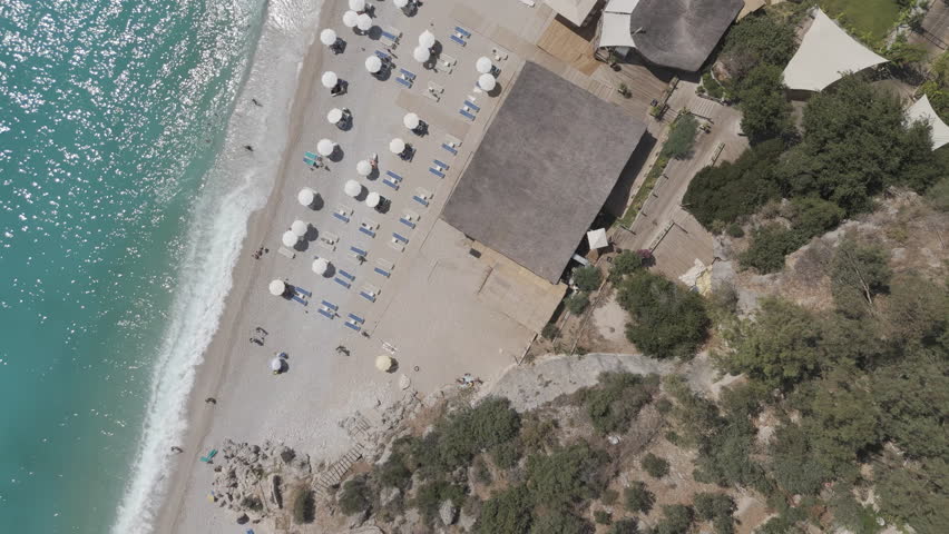 D-Log M. Oludeniz, Turkey. Aerial top down view of crowded Oludeniz Beach with rows of colorful umbrellas, many vacationers on pebble shore, sea waves crashing, summer. Aerial View, HEAD OVER SHOT