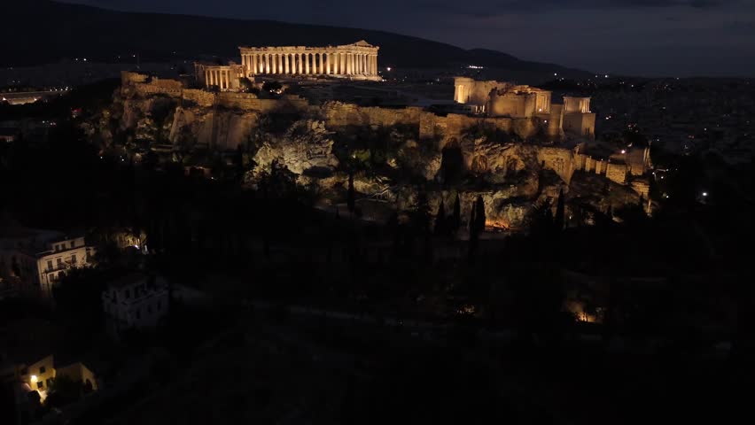 Athens, Aerial view of Beautifully illuminated Acropolis at night from a distance,drone shot approaching towards Panthenon from the side in shimmering lights.